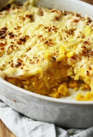Cheesy corn casserole on a wooden cutting board.