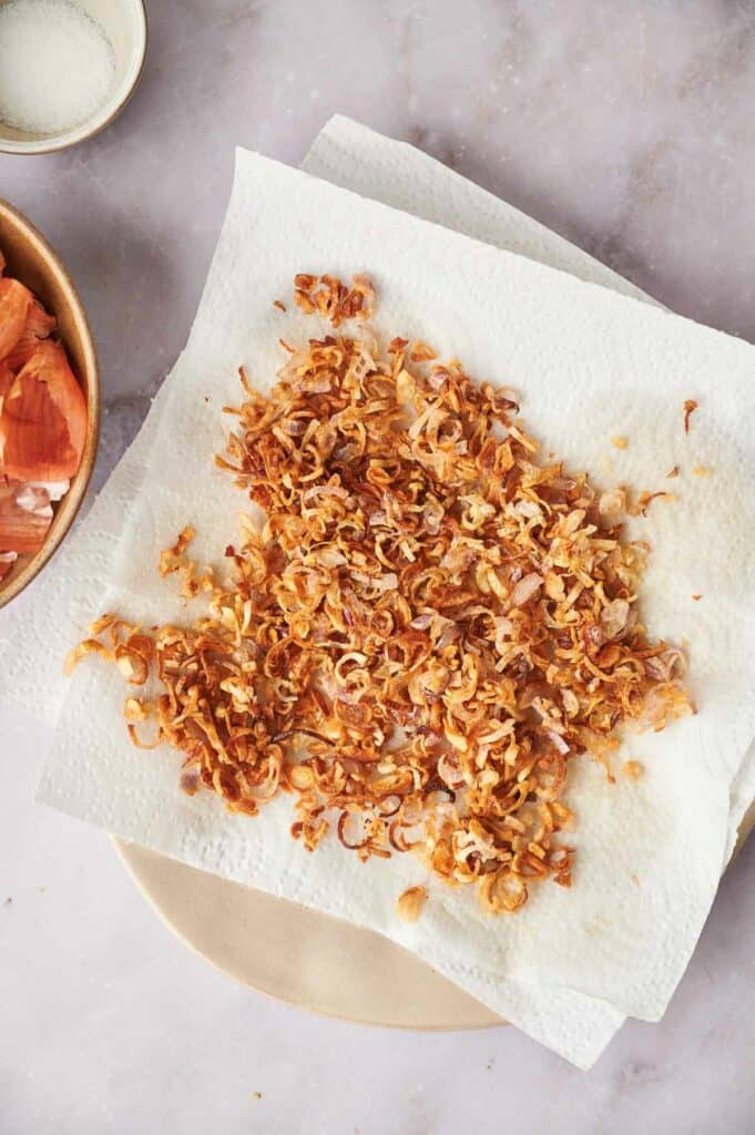 A plate with a crispy shallots on a paper towel.
