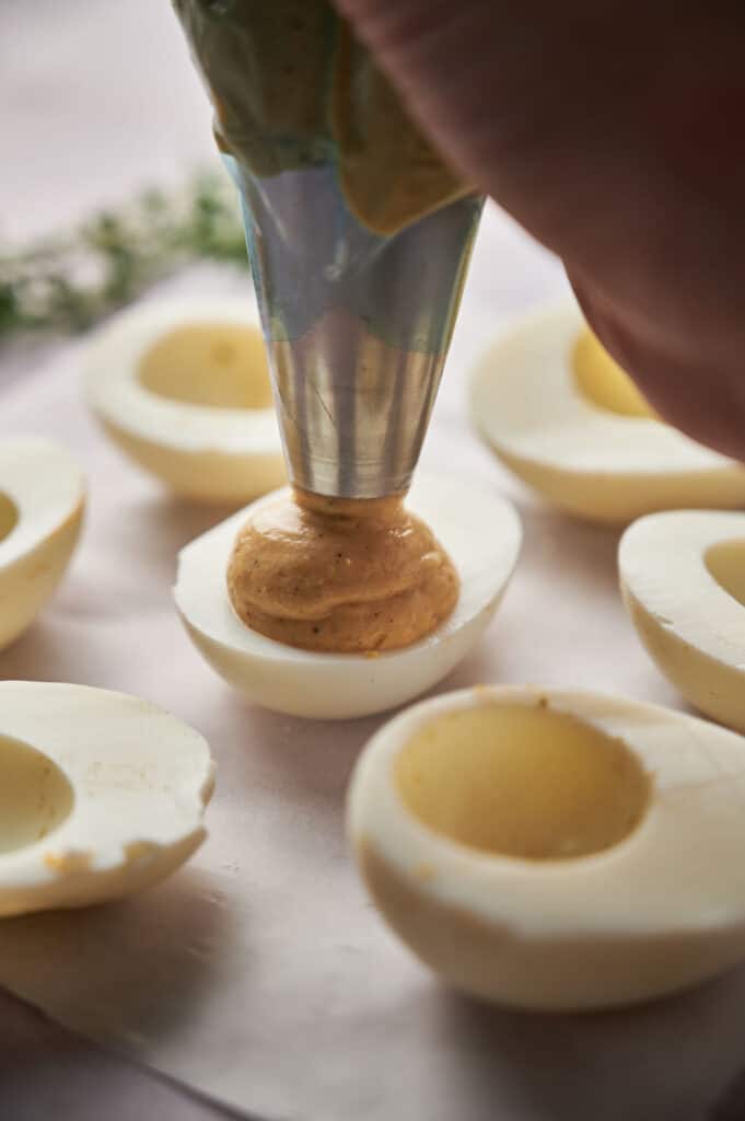 A person putting egg filling in deviled eggs.