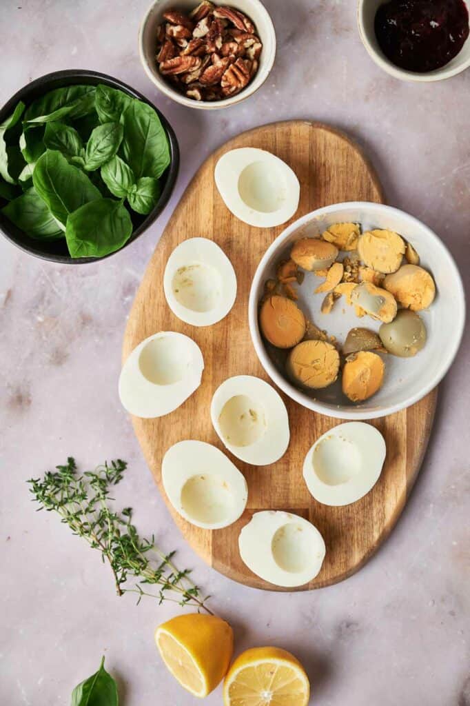 Hard boiled eggs on a cutting board with other ingredients.