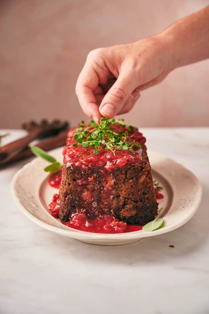A person putting a spoonful of sauce on top of a nut roast.