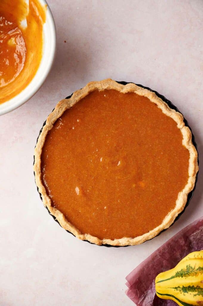 A pumpkin pie on a plate next to a bowl of pumpkin puree.