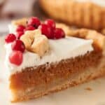 A slice of pumpkin pie on a plate with cranberries.