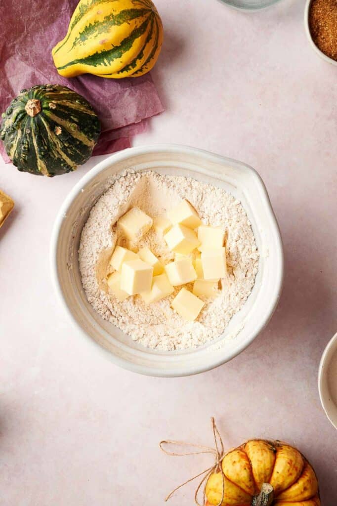 A bowl of flour, butter and pumpkins on a table.