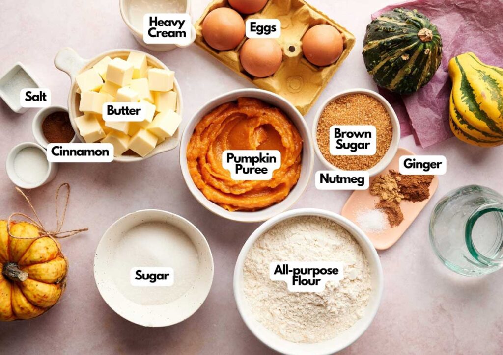 Top-down view of labeled baking ingredients for Witch Finger Cookies, including pumpkin puree, eggs, heavy cream, butter, all-purpose flour, sugars, salt, cinnamon, nutmeg, and ginger.
