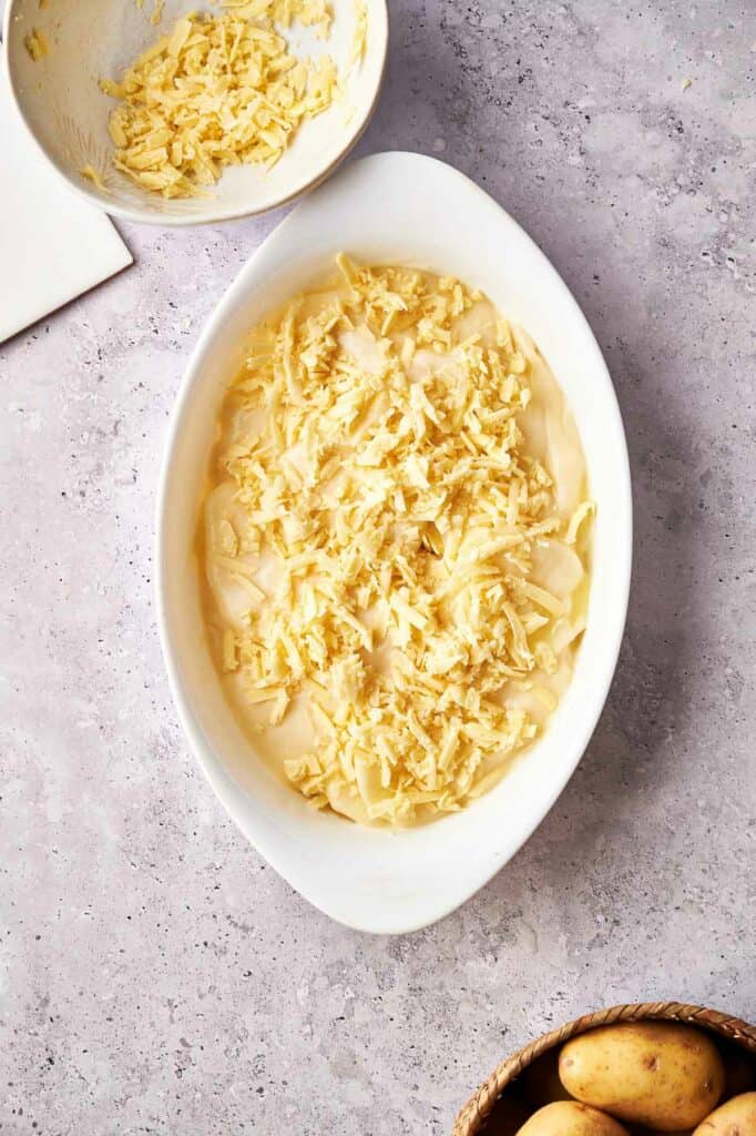 A bowl of cheesy potatoes next to a bowl of potatoes.