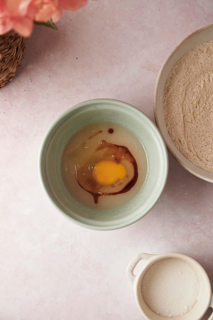 A bowl of flour and an egg on a table.