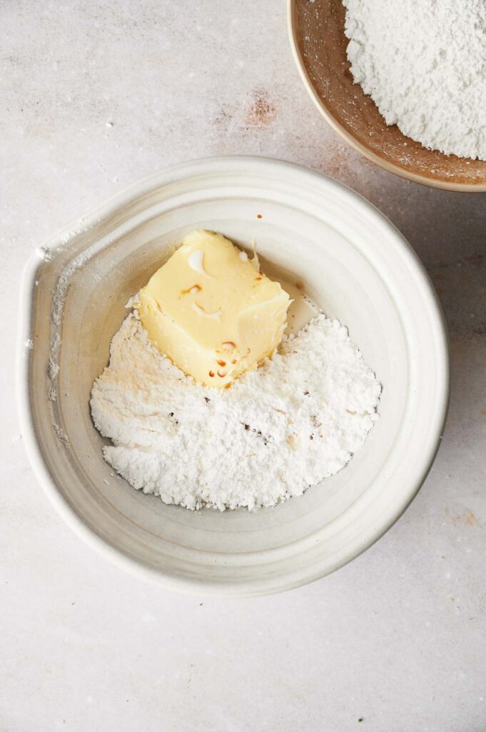 A bowl of flour and butter next to a bowl of powdered sugar.