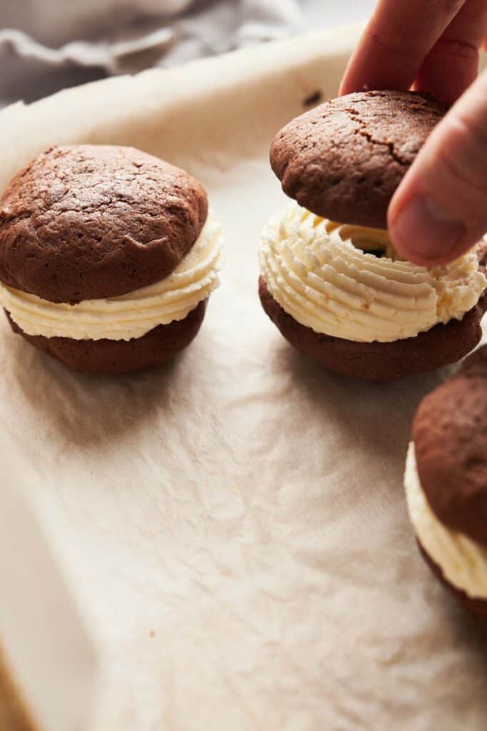 A person is putting cream on a whoopie pie.