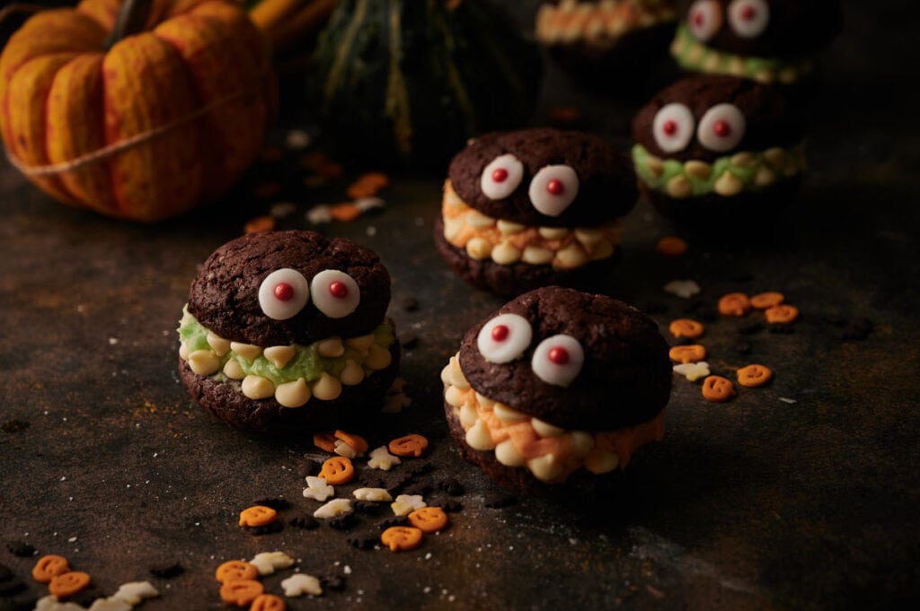A group of Whoopie pie Halloween monster cookies on a table with pumpkins.