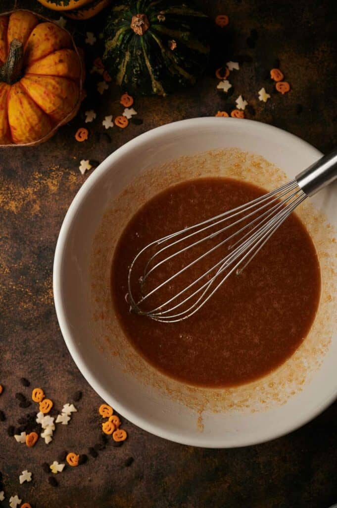 A bowl of cookie wet ingredients with a whisk and pumpkins.