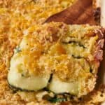 Zucchini casserole in a white dish with a wooden spoon.