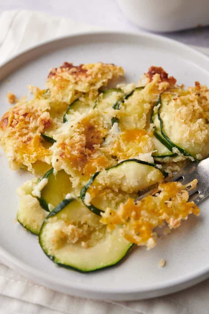 Zucchini casserole on a white plate with a fork.