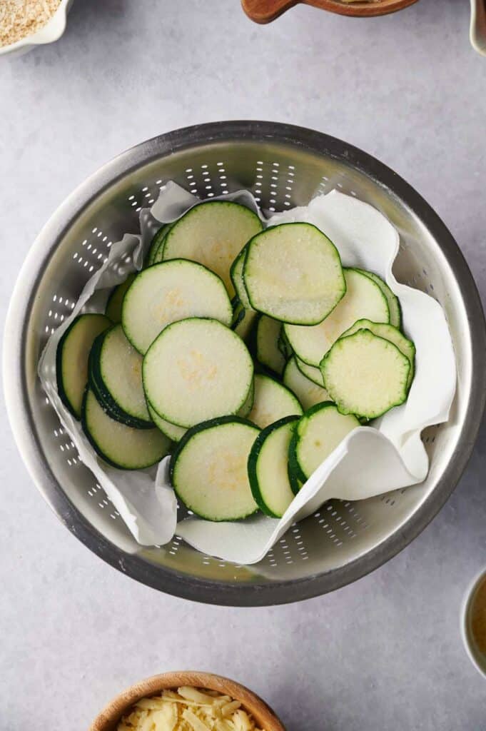 Zucchini slices in a colander on a table.