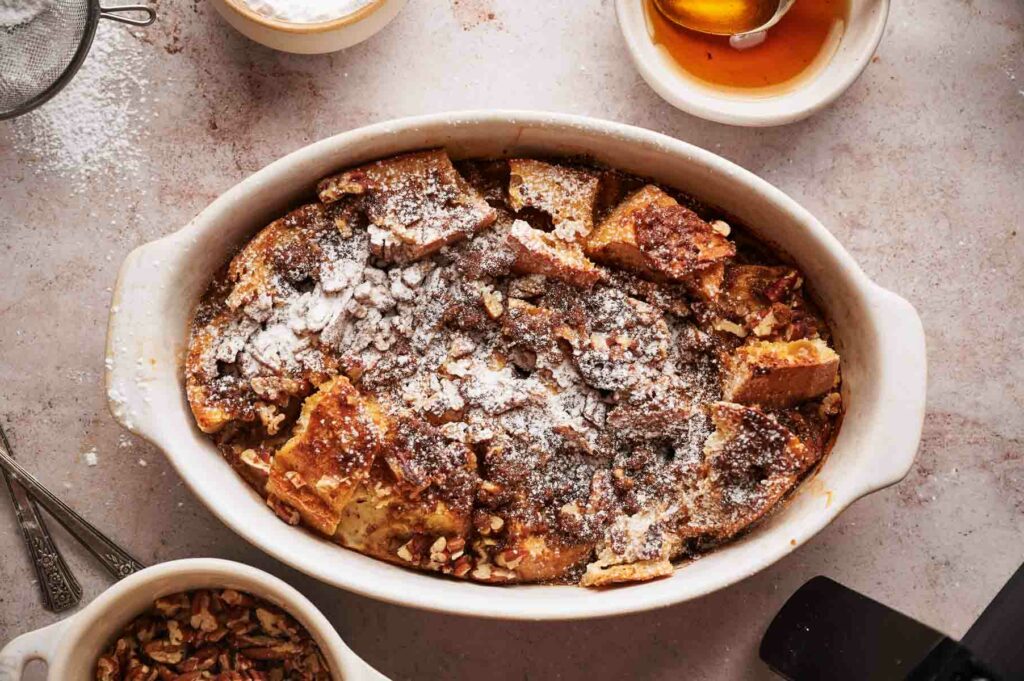 A dish of French toast casserole with powdered sugar and honey.