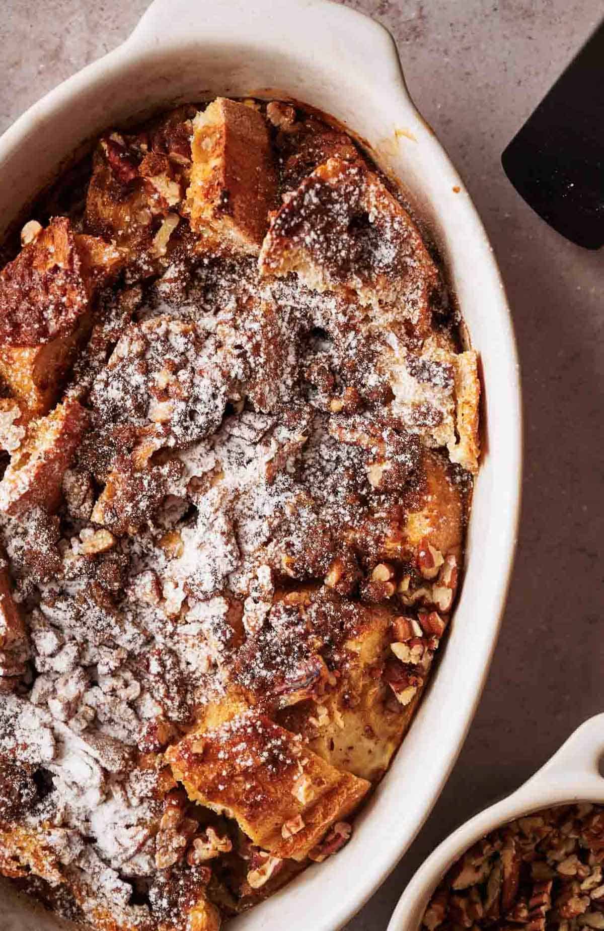 A dish of French toast casserole with pecans and powdered sugar.