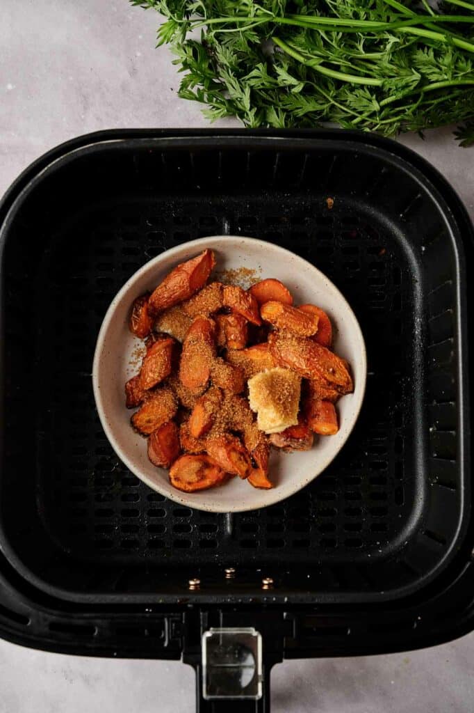 Carrots in a large bowl with butter, sugar and honey in an air fryer basket.