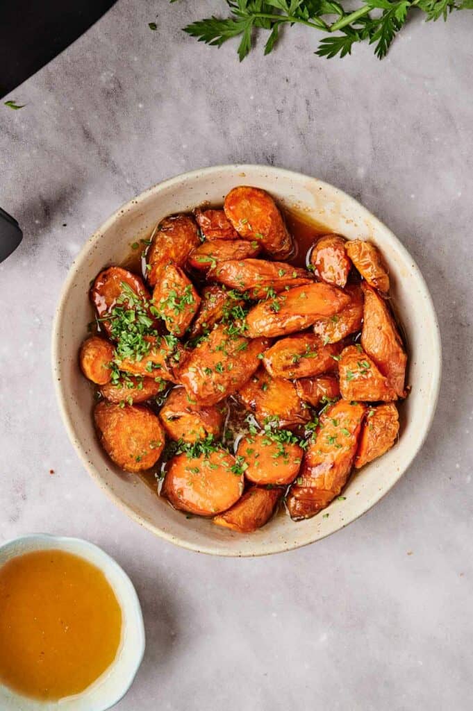 Air fryer honey glazed carrots in a bowl next to a bowl of sauce.