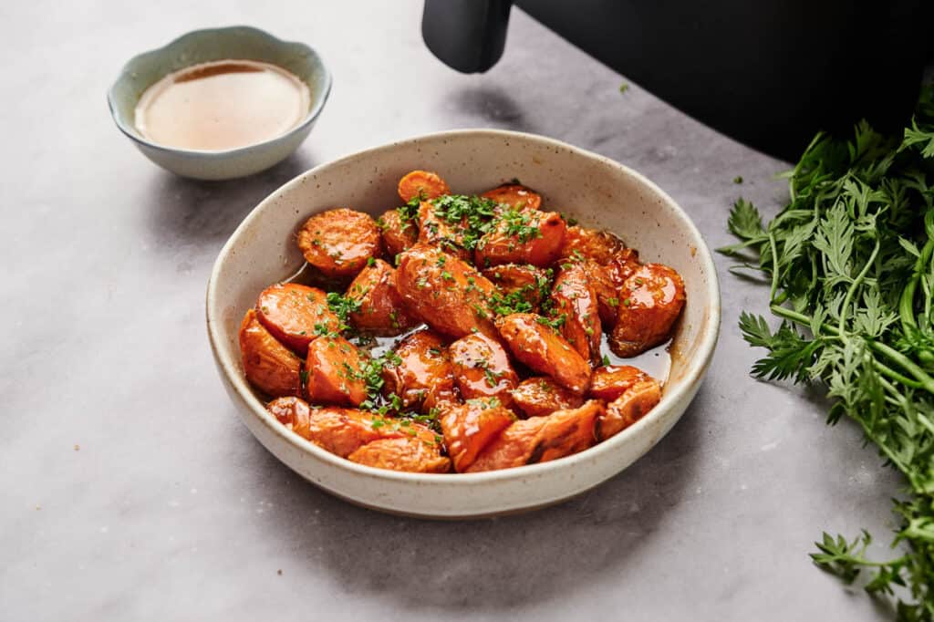 A bowl of carrots in front of an air fryer.