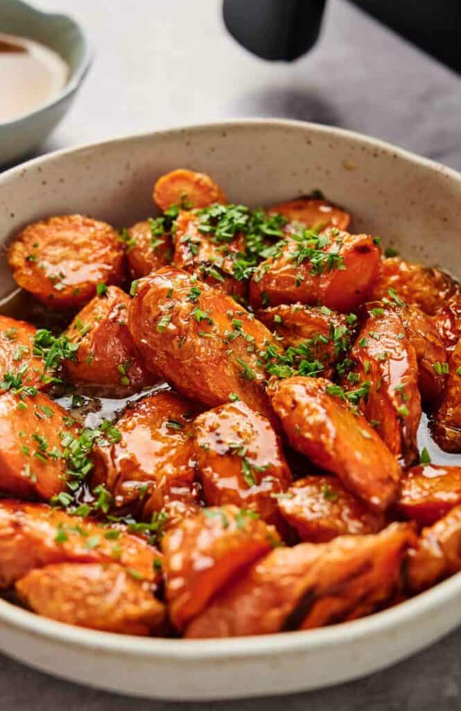 Air fryer glazed carrots in a bowl next to an air fryer.