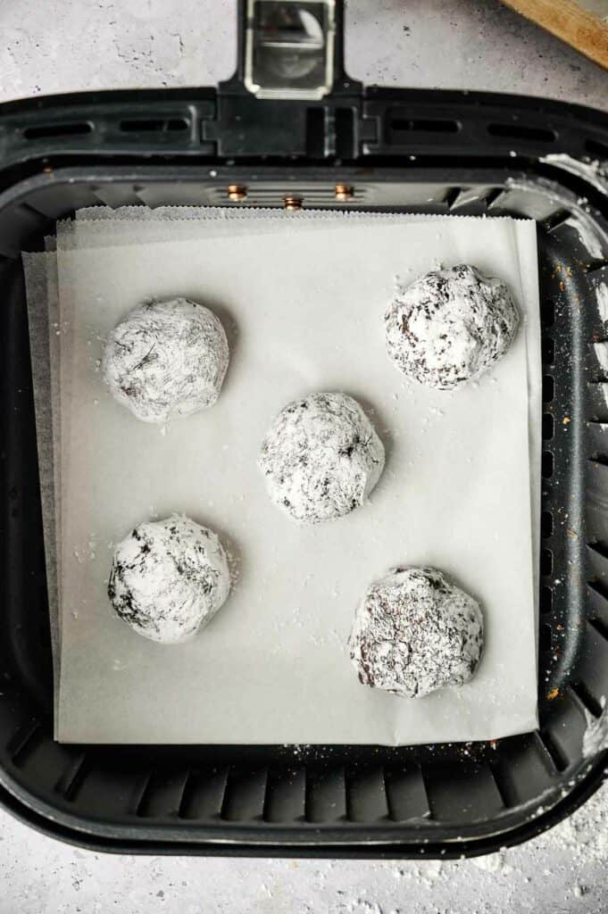 Chocolate crinkle cookies in an air fryer with powdered sugar.