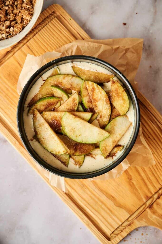 A bowl of apple slices and streusel on a wooden cutting board.