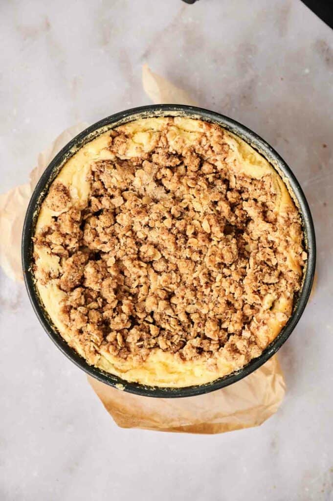 An apple pie stuffed cheesecake in a pan with a crumb topping.