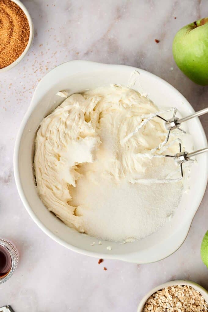 A bowl of whipped cream and apples in front of a mixer.