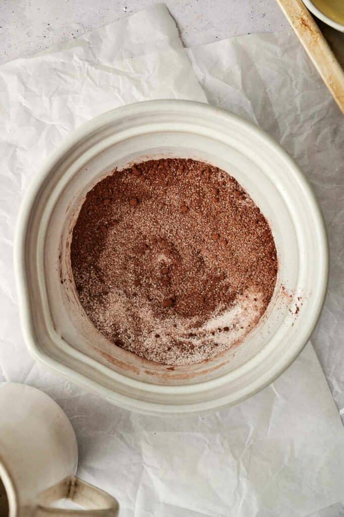 A white bowl filled with cocoa powder next to a cup of coffee.