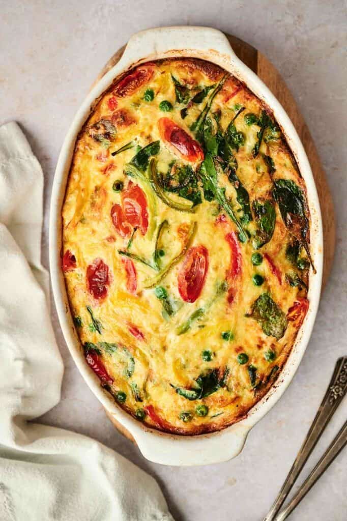 A egg and potato casserole with spinach and tomatoes in a white dish.