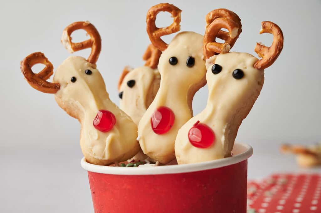 Reindeer cookie pops on sticks in a cup.