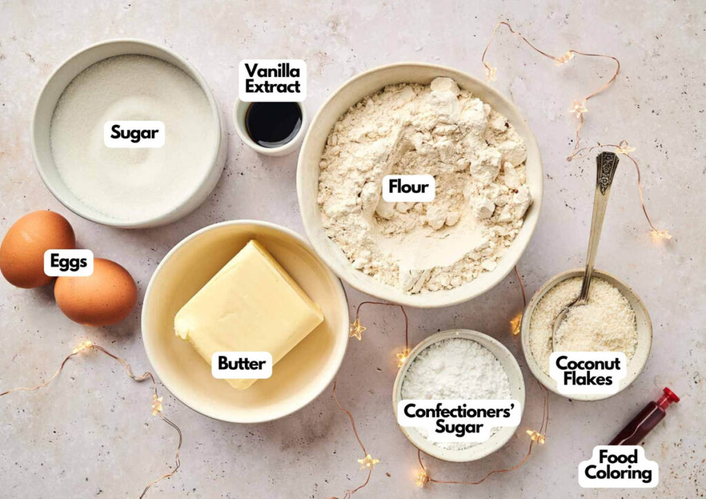 Baking ingredients on a countertop include eggs, butter, sugar, flour, vanilla extract, coconut flakes, confectioners&rsquo; sugar, food coloring, and everything you need to make an apple pie stuffed cheesecake.