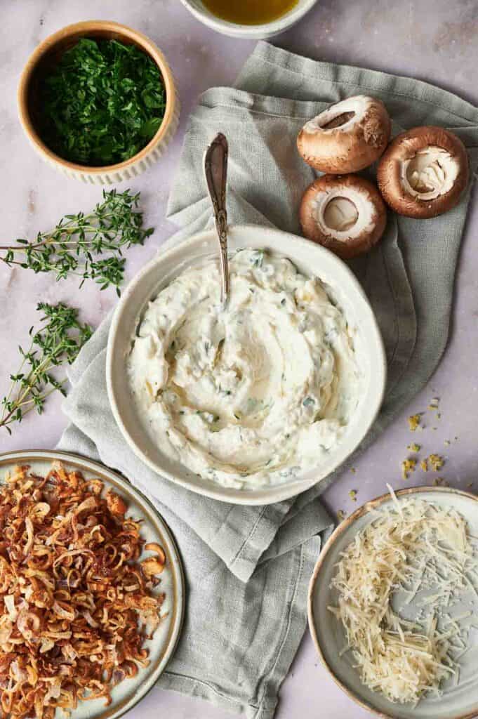 A bowl of dip with mushrooms and herbs on a table.