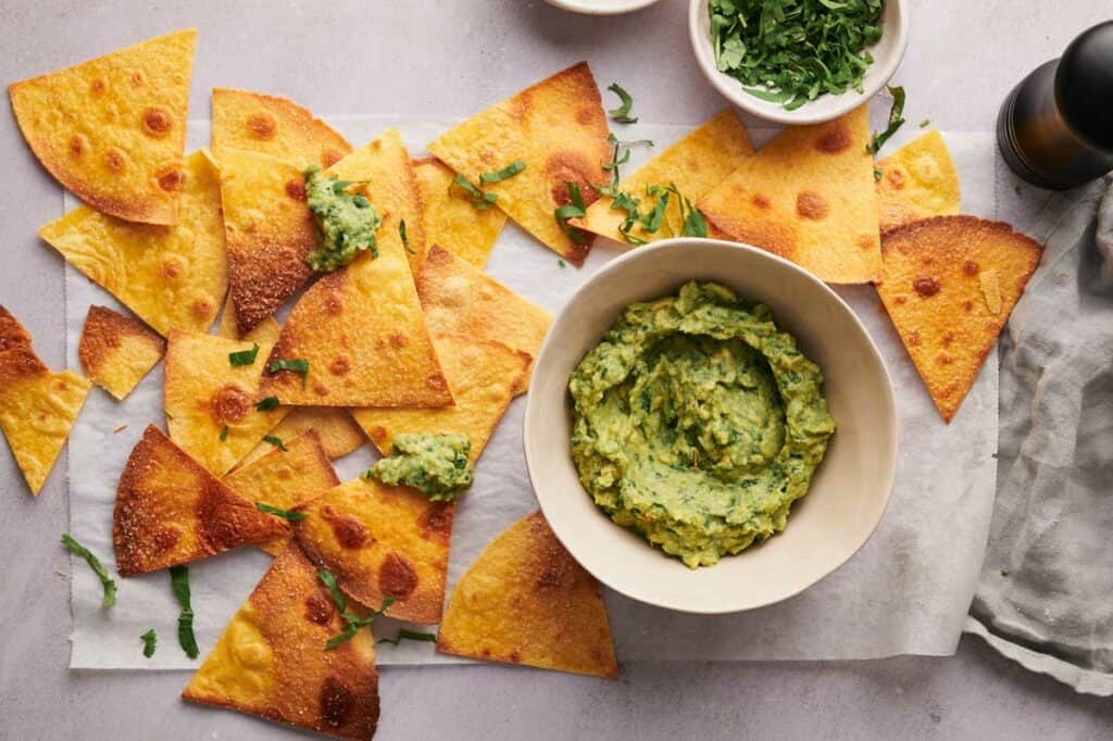 A plate of tortilla chips with guacamole and a pepper grinder.