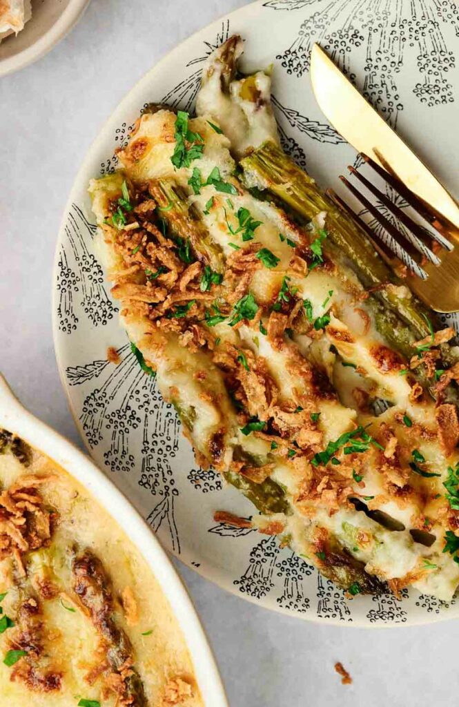 A plate of cheesy asparagus casserole with a fork and knife.