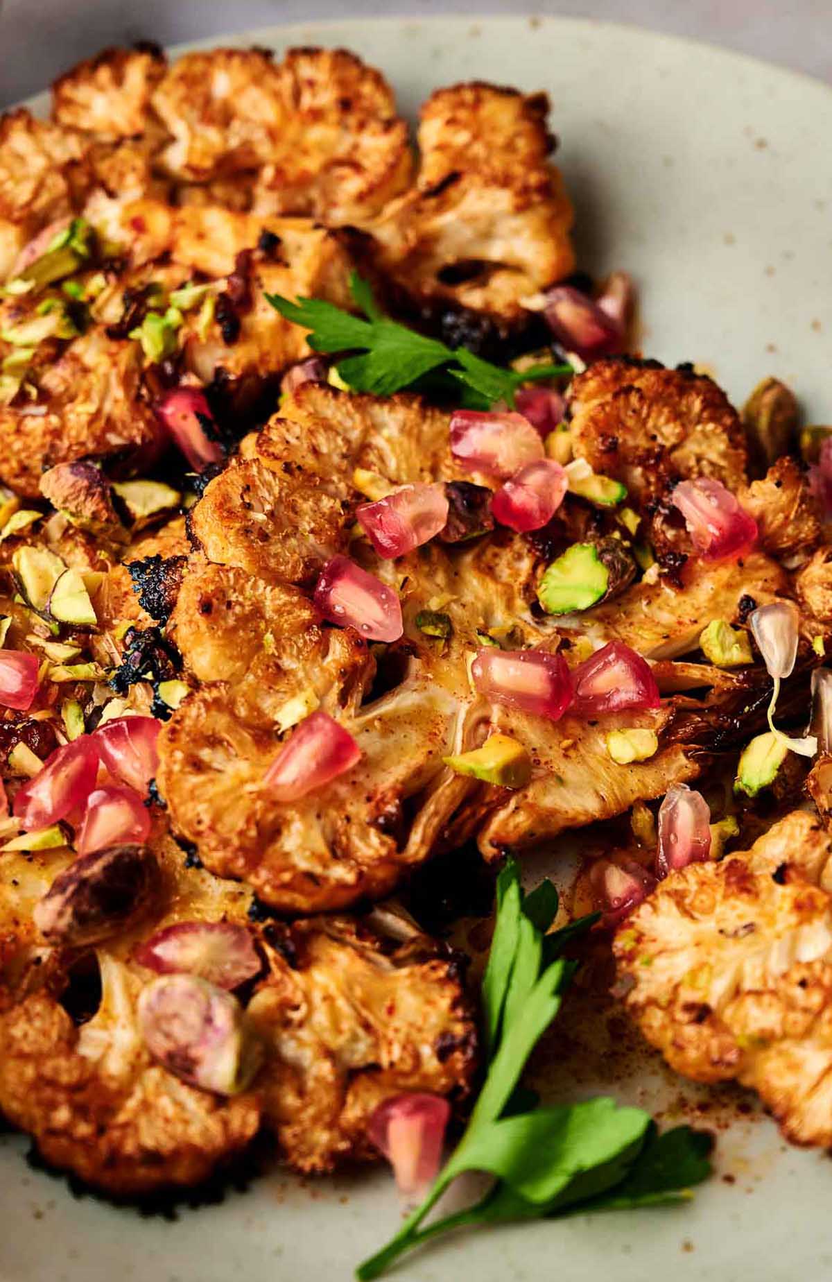 A delicious plate of cauliflower steaks, beautifully garnished with pomegranate and pistachios.