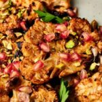 A delicious plate of cauliflower steaks, beautifully garnished with pomegranate and pistachios.