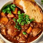 A bowl of vegetable stew with bread on the side.
