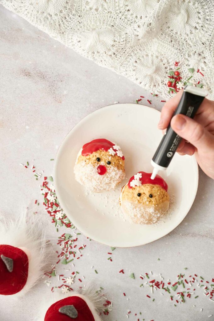 A person is making santa cookies on a plate.