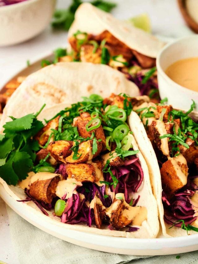 Chicken tacos on a white plate with slaw and sauce.