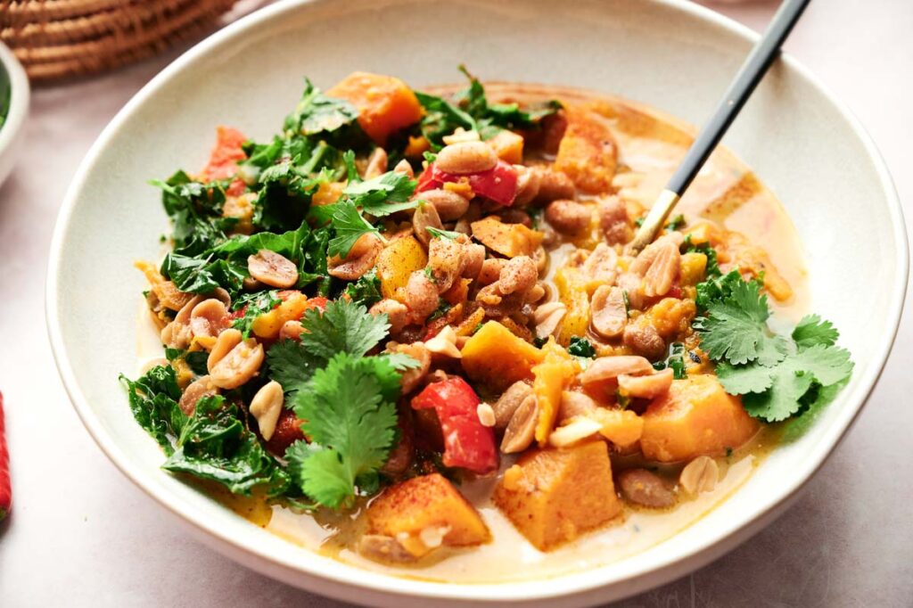 A bowl of Thai peanut curry with sweet potato and kale.