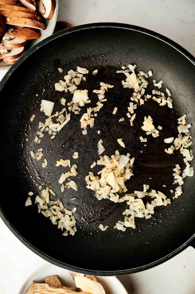 A skillet with onion and garlic for a wild rice casserole dish.