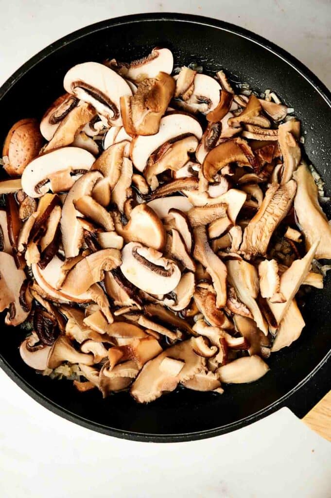 A skillet with onion, garlic, and mushrooms for a wild rice casserole dish.