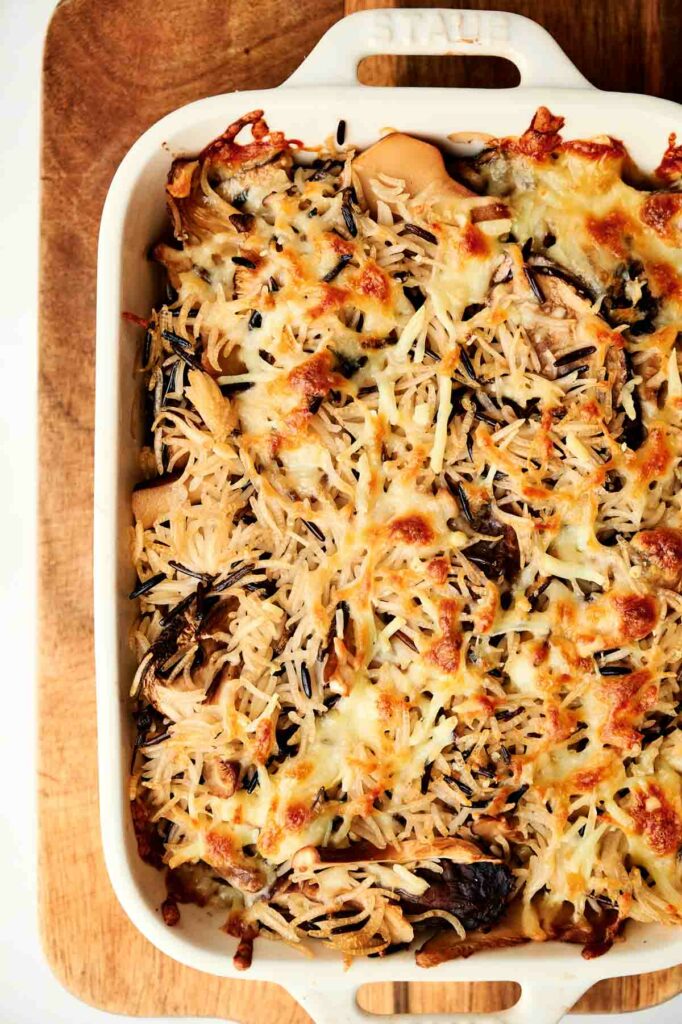 A wild rice casserole dish with cheese and mushrooms on top.