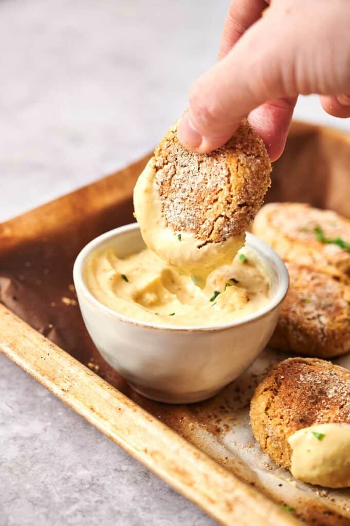 A person dipping chickpea nuggets into a sauce bowl.