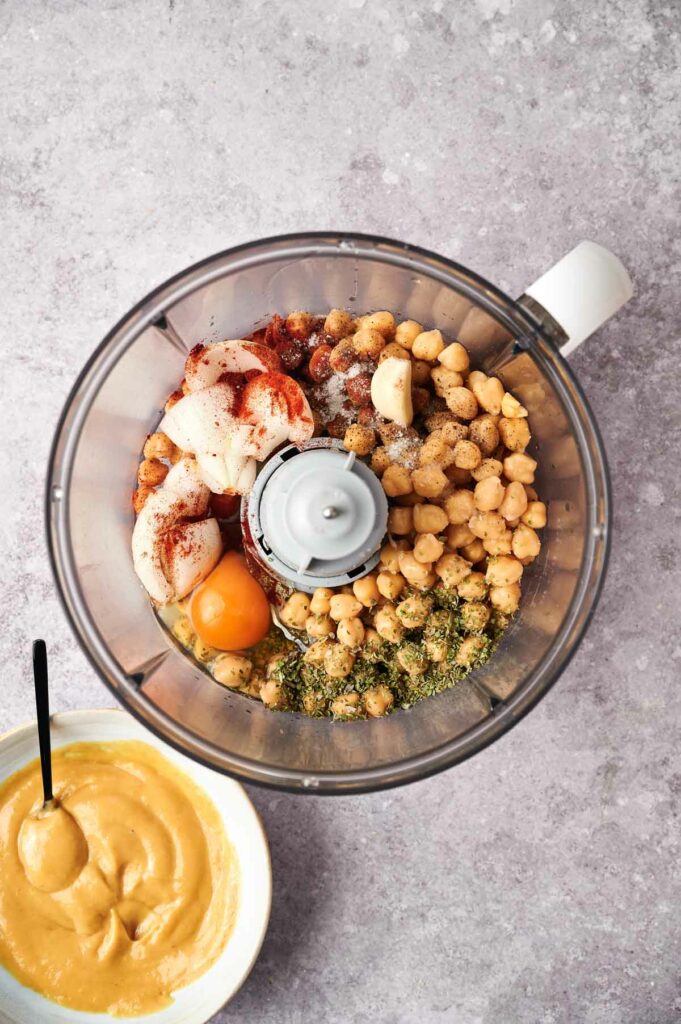 A food processor filled with chickpea nuggets and a bowl of hummus.