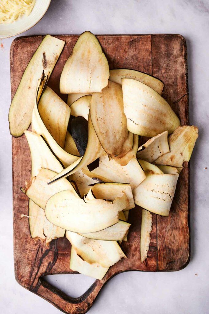 A pile of sliced eggplant on a cutting board.