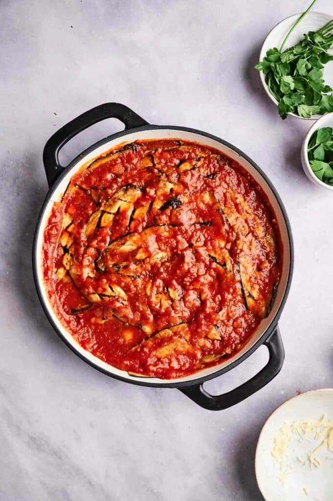 A pot of eggplant casserole with a couple bowls of parsley.