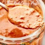 A spoonful of chunky Thai red curry sauce being lifted from a jar.