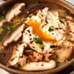 A bowl of Korean tofu soup with vegetables and eggs.